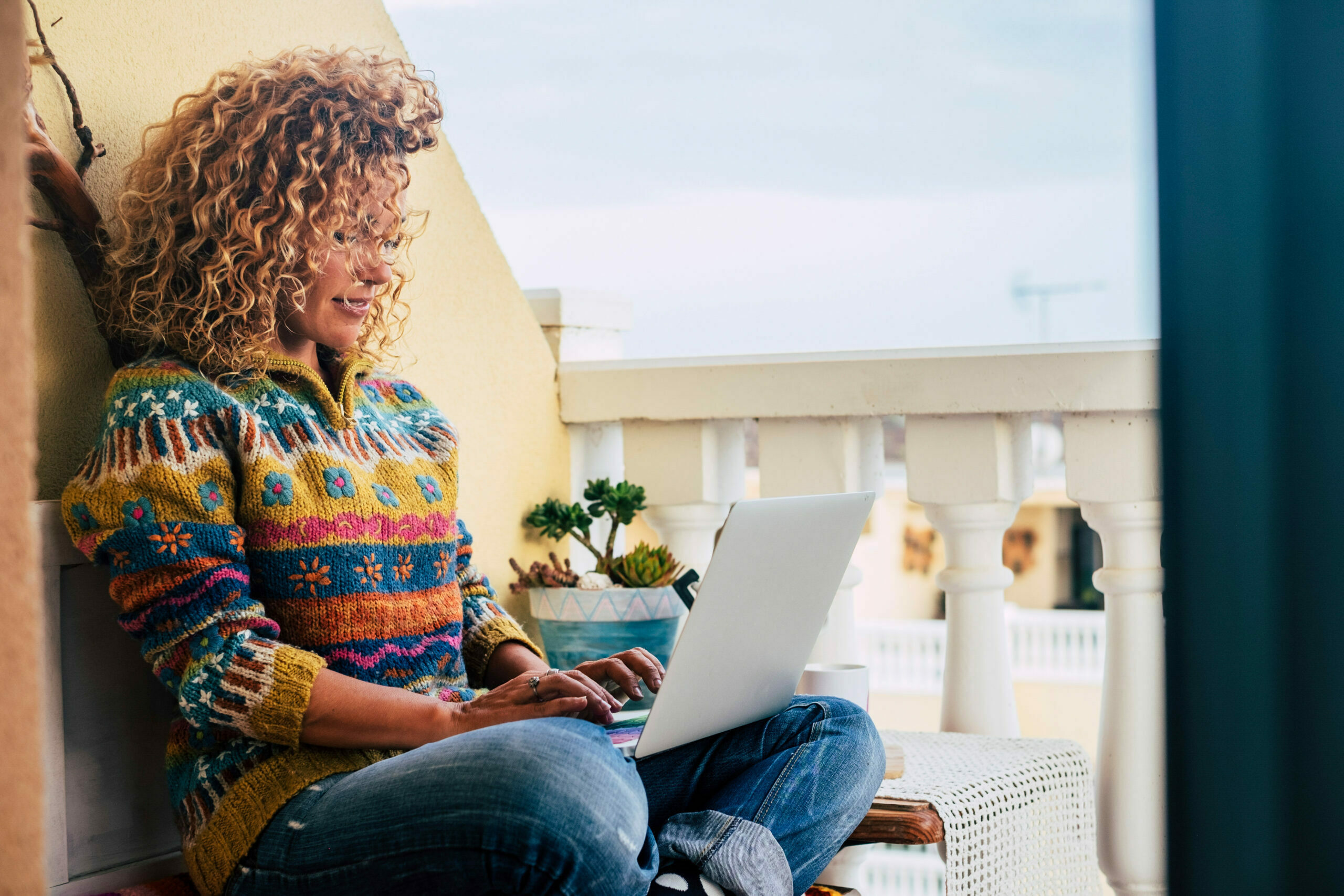 Woman in a colorful sweater with laptop working on balcony