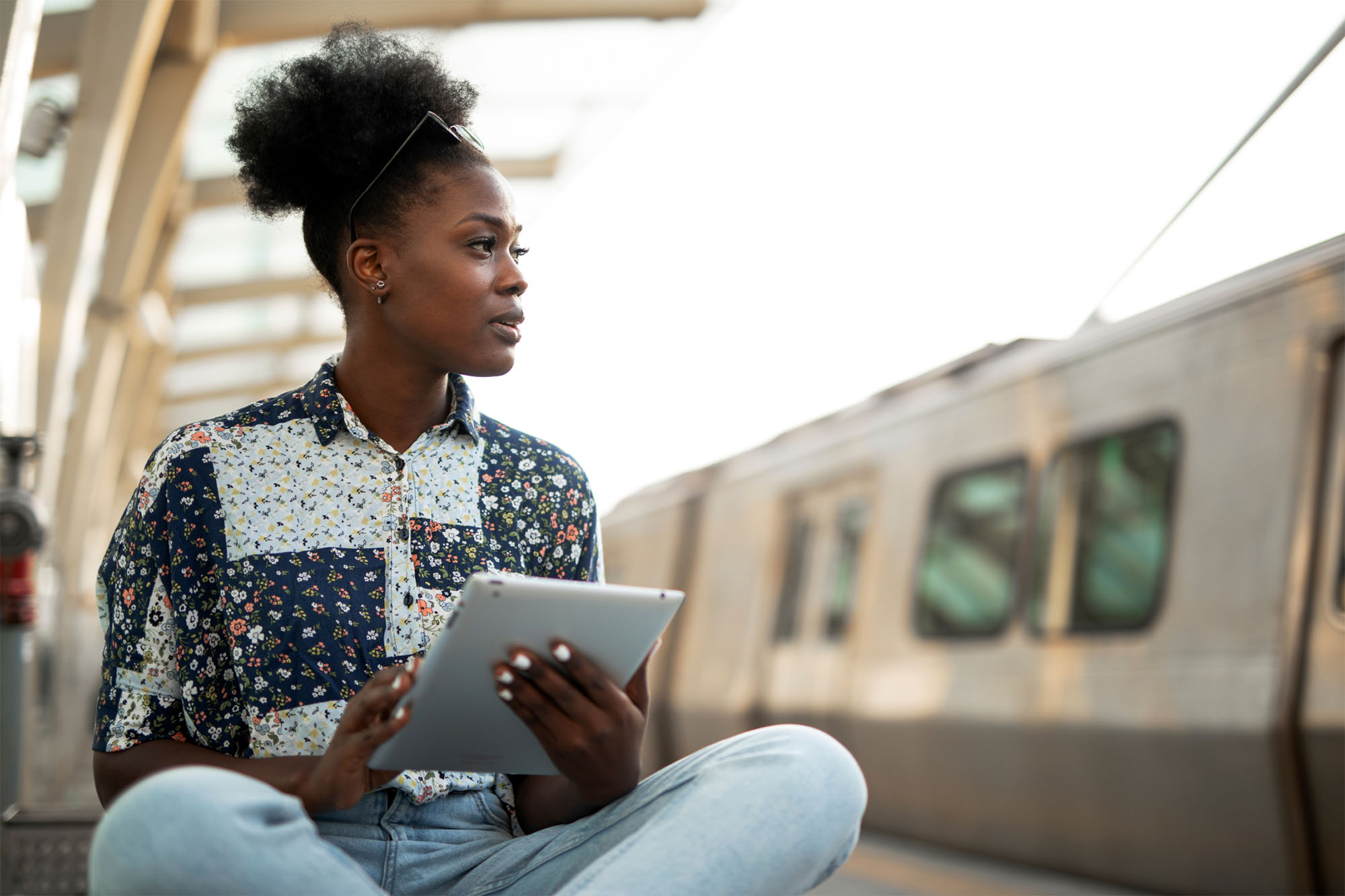 young woman sitting down on train station looking at a Digital Sales Room on her tablet